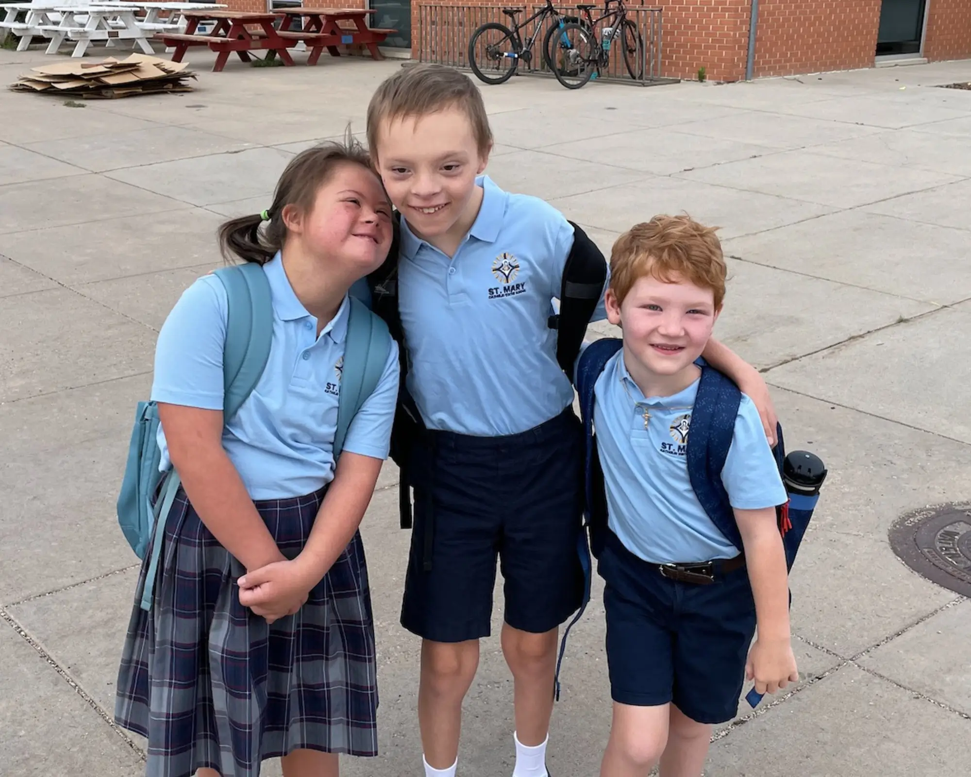 Three smiling students in St. Mary school uniforms standing arm in arm outside their school
